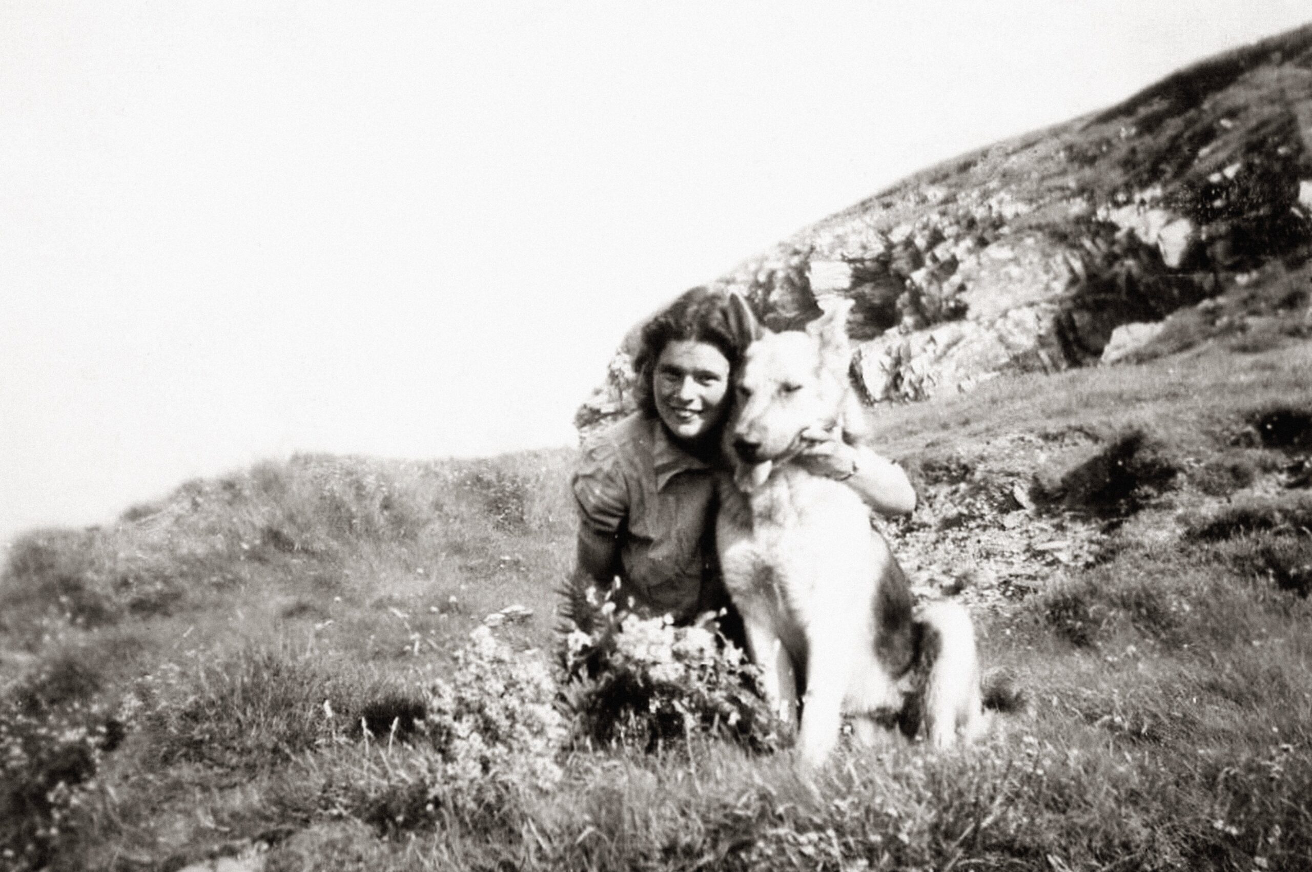 A touching vintage photo of a woman with a dog in a mountainous landscape.