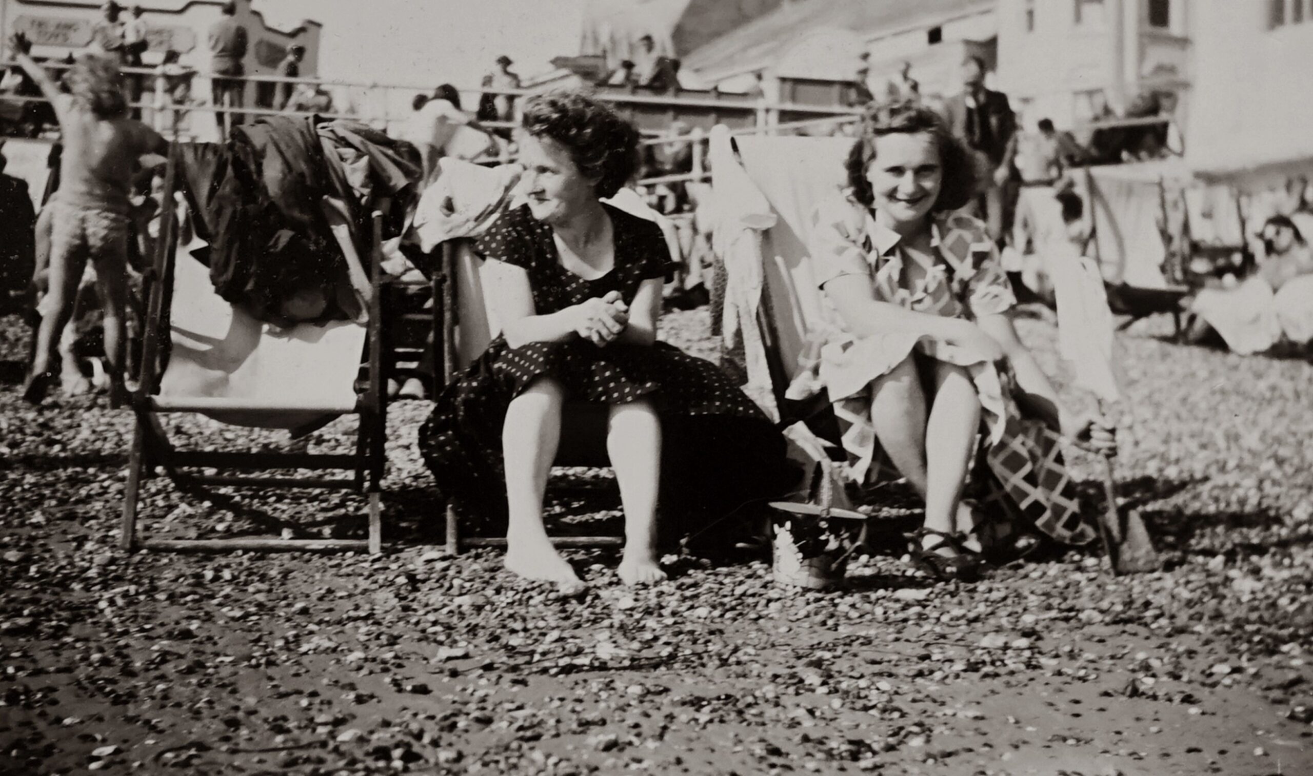 Black and white vintage photo of women sitting on beach chairs in a lively setting.