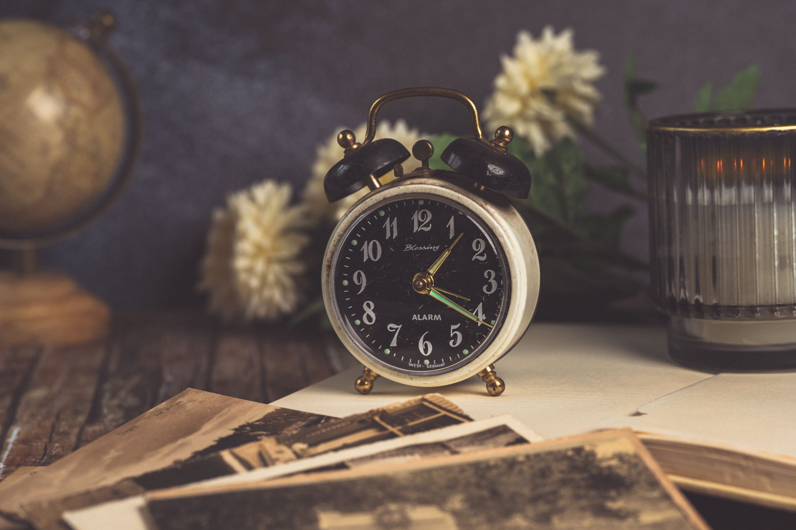 Classic analogue alarm clock with postcards, candle, globe, and flowers.